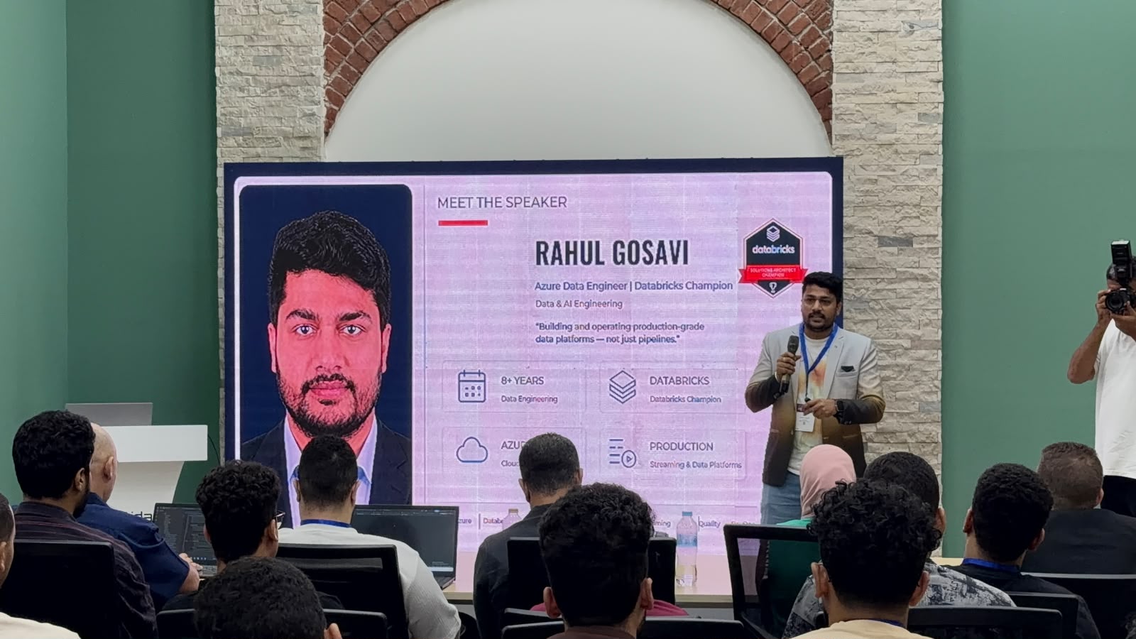 Rahul Gosavi speaking to the audience in front of the 'Meet the Speaker' slide at DevOpsDays Cairo 2026